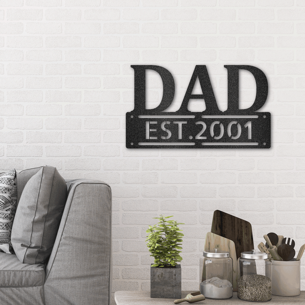 Personalized metal wall art sign of the word DAD in bold writing. You can personalize the row underneath it with a name or date. Use this as a gift for Father's Day. This picture shows the design in the color black hanging on the wall in the living room.