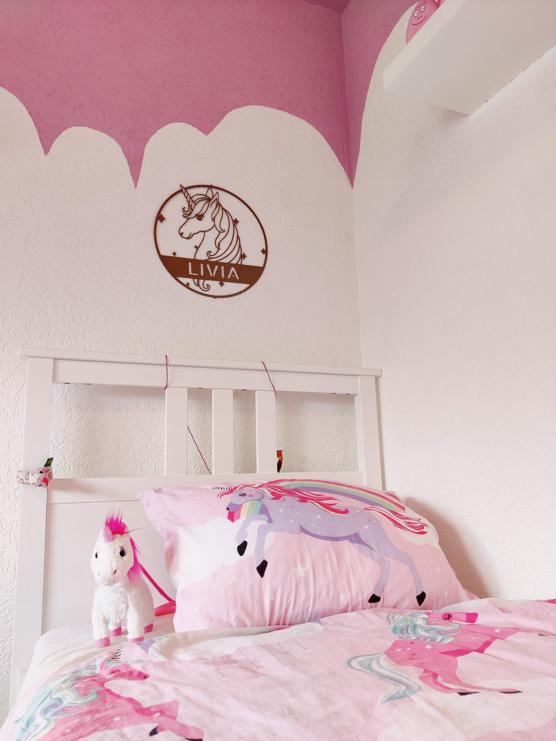 Girls bedroom with the a metall wall art sign of a cute unicorn with the name of the daugther on it. Hanging on the wall above the bed. This steel sign is powder coated in the color gold.