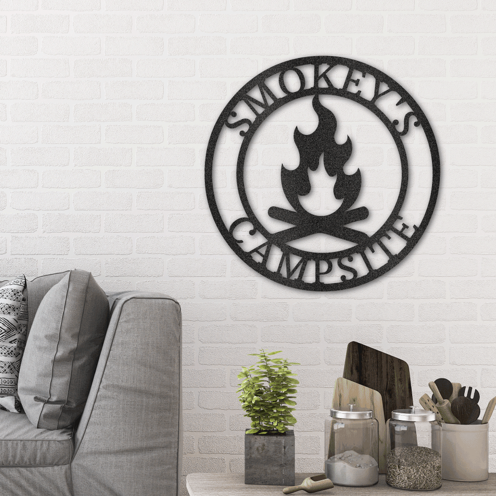 Metal Wall Art Sign of a campfire inside a ring. In the ring you can add personalized names or text. The picture shows the steel design in the color black hanging in a living room as home decor above a couch
