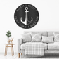 Round metal wall sign with a anchor in the middle. Around there is place to customize it with your names or any text. In the color black hanging on the wall above a couch.