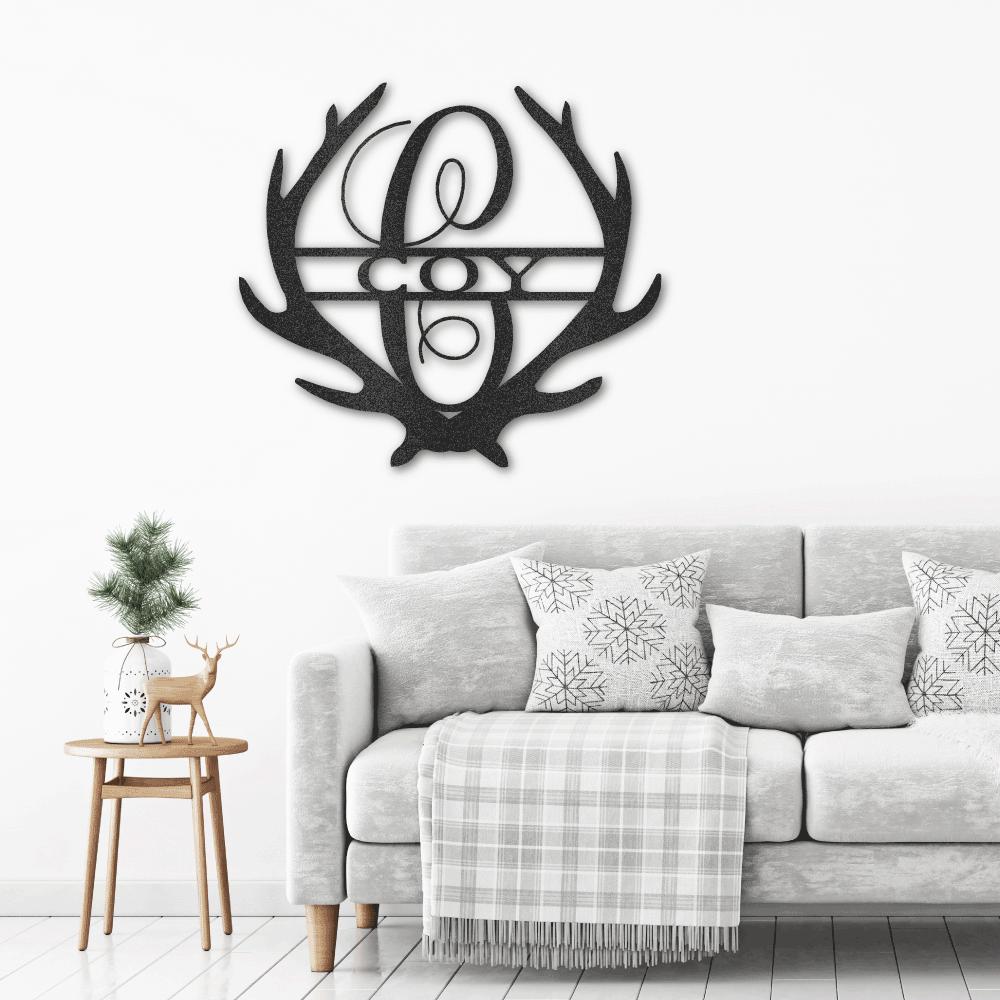 Metal Wall Art Sign of two antlers with a monogram and name inside in the color black hanging on the wall above a couch